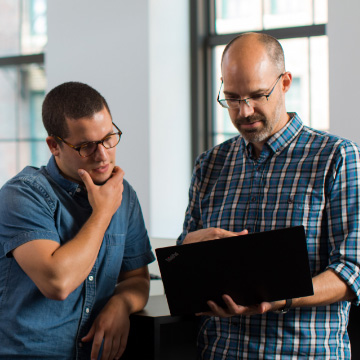 ISV developers working together to deploy an app, both men stand in the middle of an office looking at one computer